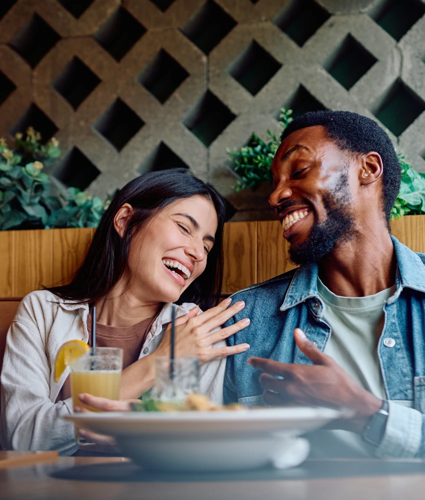 Un couple heureux rit librement tout en partageant un repas, montrant l'habitude de construire un mariage pour la vie
