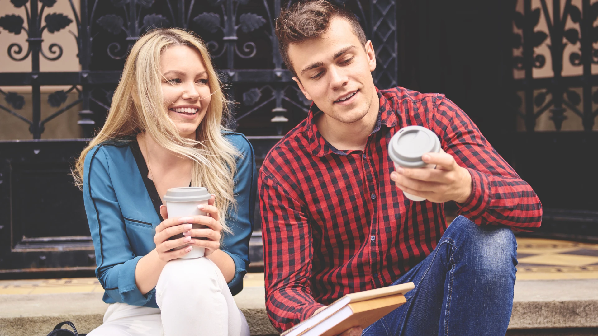 Jeune couple intelligent souriant sur un perron tout en buvant des cafés