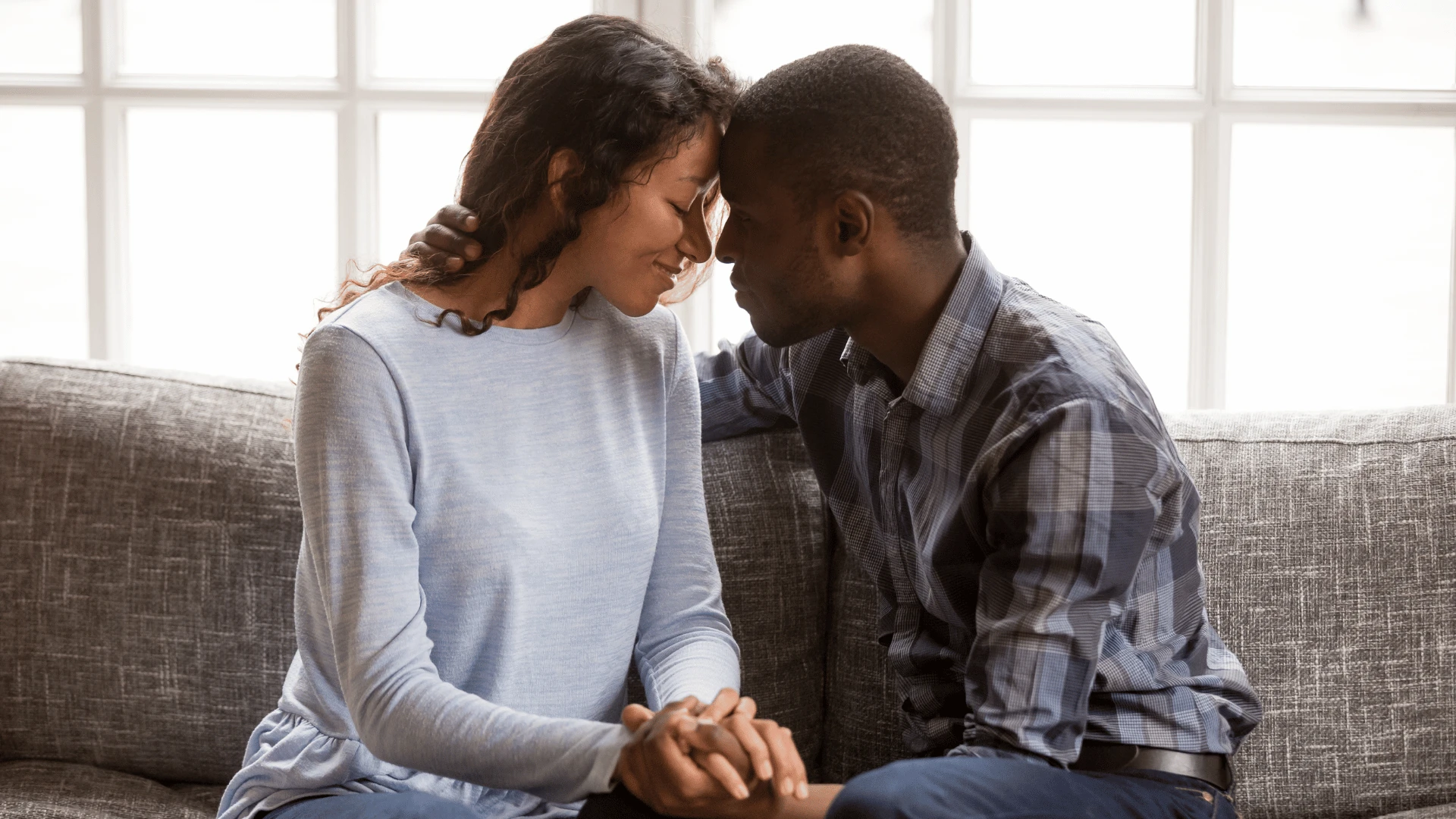 Homme exceptionnellement intelligent touchant le front de la femme qu'il aime près d'une fenêtre lumineuse